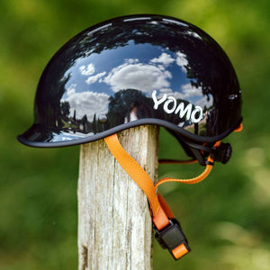 YOMO glossy dark grey kids' helmet perched on a wooden post against a blurred, natural background.