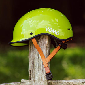 YOMO glossy green kids' helmet perched on a wooden post against a blurred, natural background.