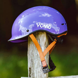 YOMO glossy purple kids' helmet perched on a wooden post against a blurred, natural background.