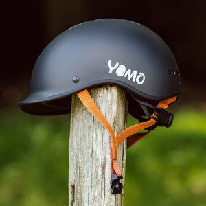 YOMO matt dark grey kids' helmet perched on a wooden post against a blurred, natural background.