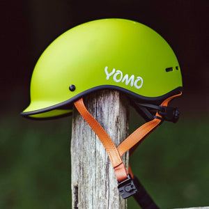 YOMO matt green kids' helmet perched on a wooden post against a blurred, natural background.