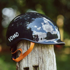 YOMO glossy dark grey kids' helmet perched on a wooden post against a blurred, natural background.