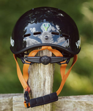 YOMO glossy dark grey kids' helmet perched on a wooden post against a blurred, natural background.