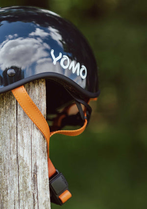 YOMO glossy dark grey kids' helmet perched on a wooden post against a blurred, natural background.