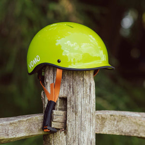 YOMO glossy green kids' helmet perched on a wooden post against a blurred, natural background.
