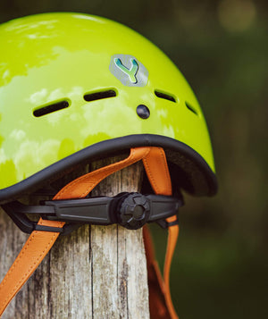 YOMO glossy green kids' helmet perched on a wooden post against a blurred, natural background.