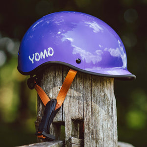 YOMO glossy purple kids' helmet perched on a wooden post against a blurred, natural background.