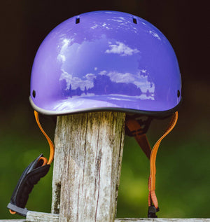 YOMO glossy purple kids' helmet perched on a wooden post against a blurred, natural background.