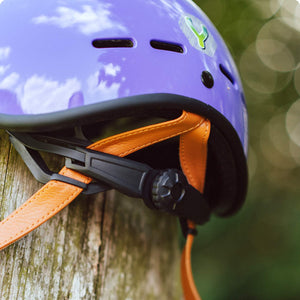 YOMO glossy purple kids' helmet perched on a wooden post against a blurred, natural background.