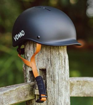 YOMO matt dark grey kids' helmet perched on a wooden post against a blurred, natural background.