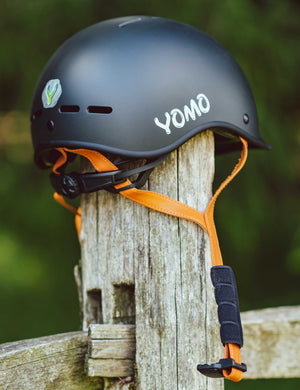 YOMO matt dark grey kids' helmet perched on a wooden post against a blurred, natural background.