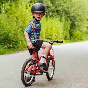 Child wearing a YOMO matt dark grey kids' helmet on a red YOMO bike on a road with greenery in the background.
