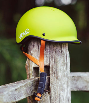 YOMO matt green kids' helmet perched on a wooden post against a blurred, natural background.