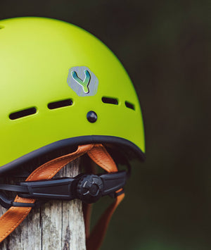 YOMO matt green kids' helmet perched on a wooden post against a blurred, natural background.