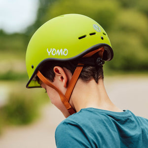 Child wearing a YOMO matt green kids' helmet outdoors against a blurred, natural background.