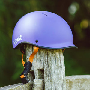 YOMO matt purple kids' helmet perched on a wooden post against a blurred, natural background.
