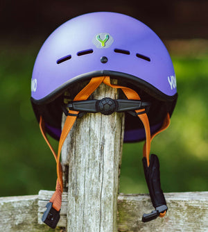 YOMO matt purple kids' helmet perched on a wooden post against a blurred, natural background.