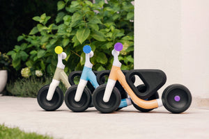 Three Woom WOW balance bikes with colourful handles parked outdoors.